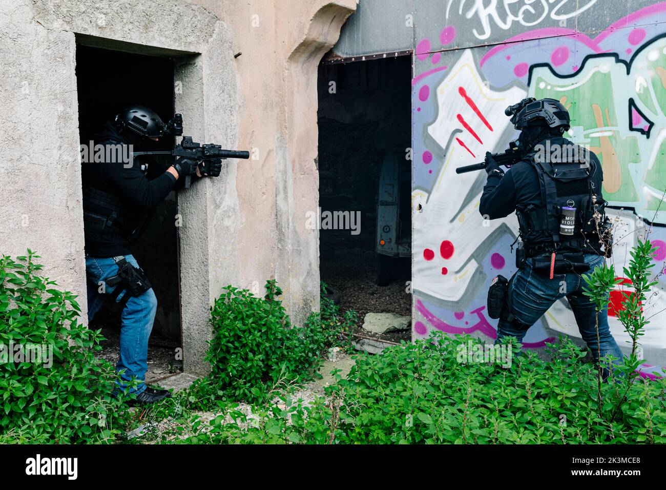 Corps complet de combattants des forces spéciales non reconnaissables en équipement de combat et casques de protection visant avec des fusils modernes près du vieux bâtiment avec graffiti wa Banque D'Images