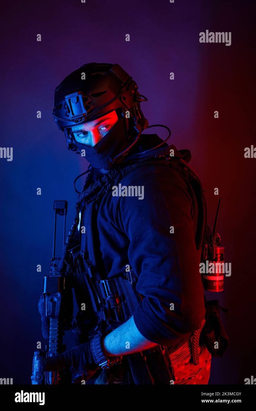 Inreconnaissable, un jeune homme de combat attentif dans un équipement de combat et un casque de protection qui regarde loin dans une pièce sombre Banque D'Images