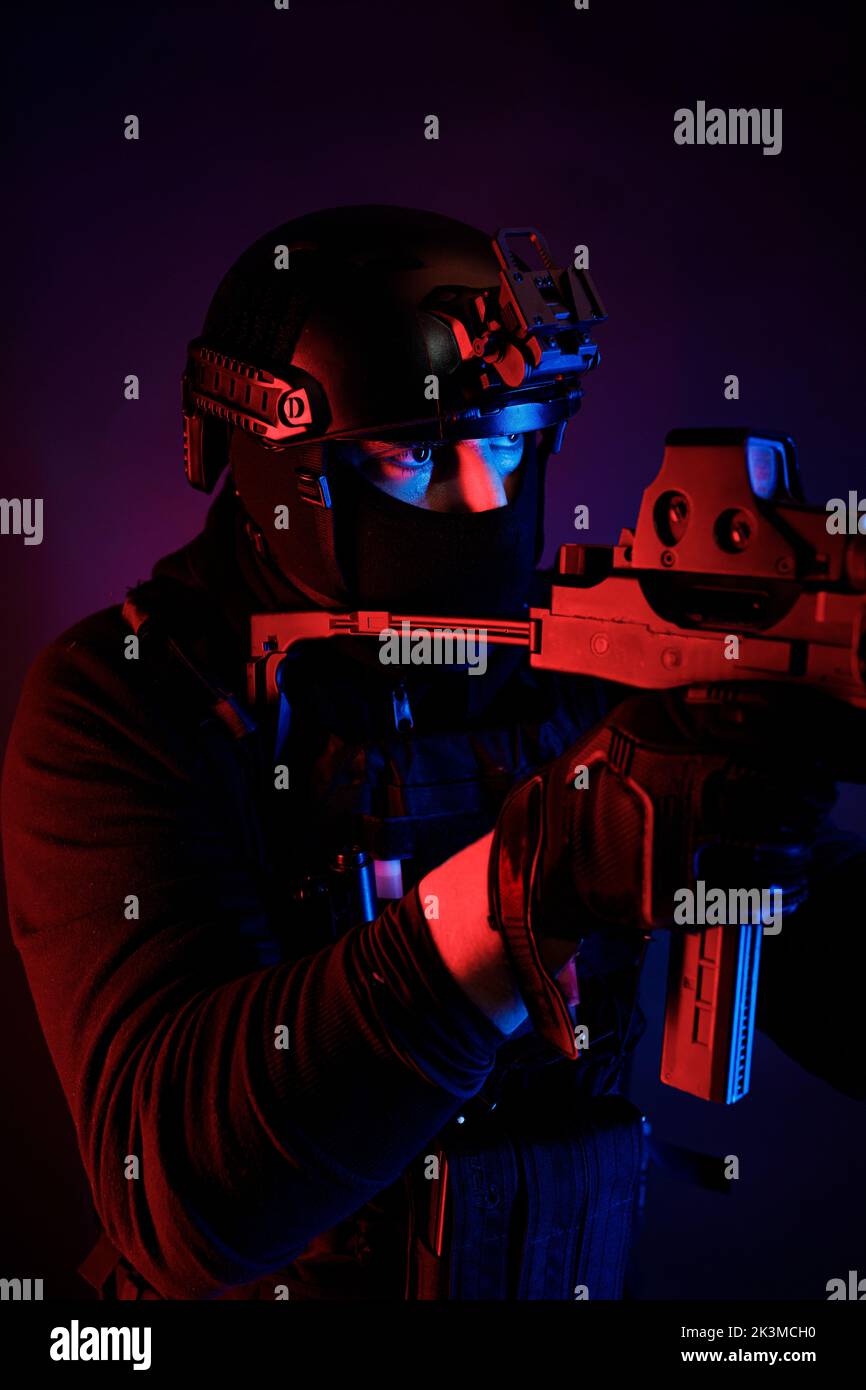 Inreconnaissable un jeune homme de combat attentif dans un équipement de combat et un casque de protection regardant loin à travers la lentille du fusil tout en prenant le but dans la pièce sombre Banque D'Images