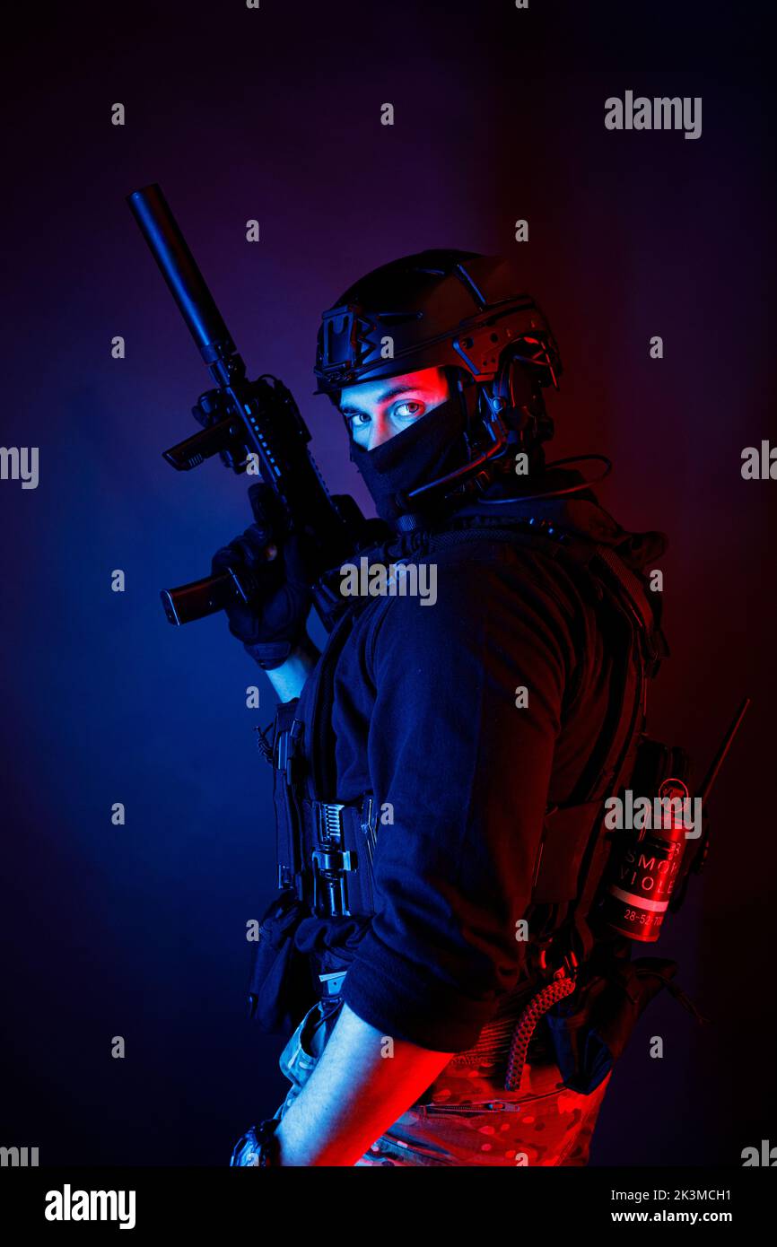 Inreconnaissables un jeune homme attentif dans un équipement de combat et un casque de protection regardant la caméra dans une pièce sombre Banque D'Images