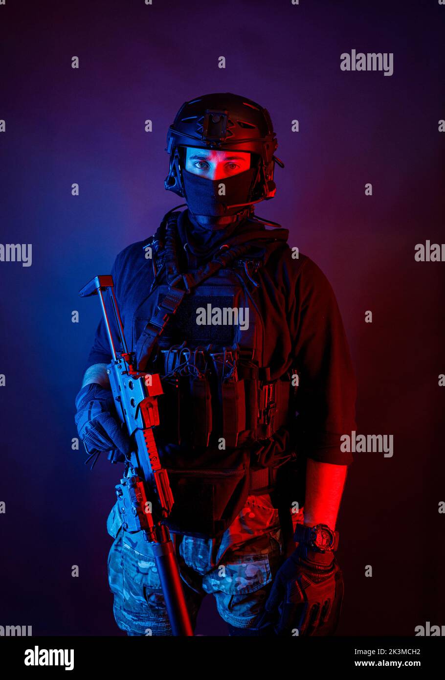 Inreconnaissables un jeune homme attentif dans un équipement de combat et un casque de protection regardant la caméra dans une pièce sombre Banque D'Images