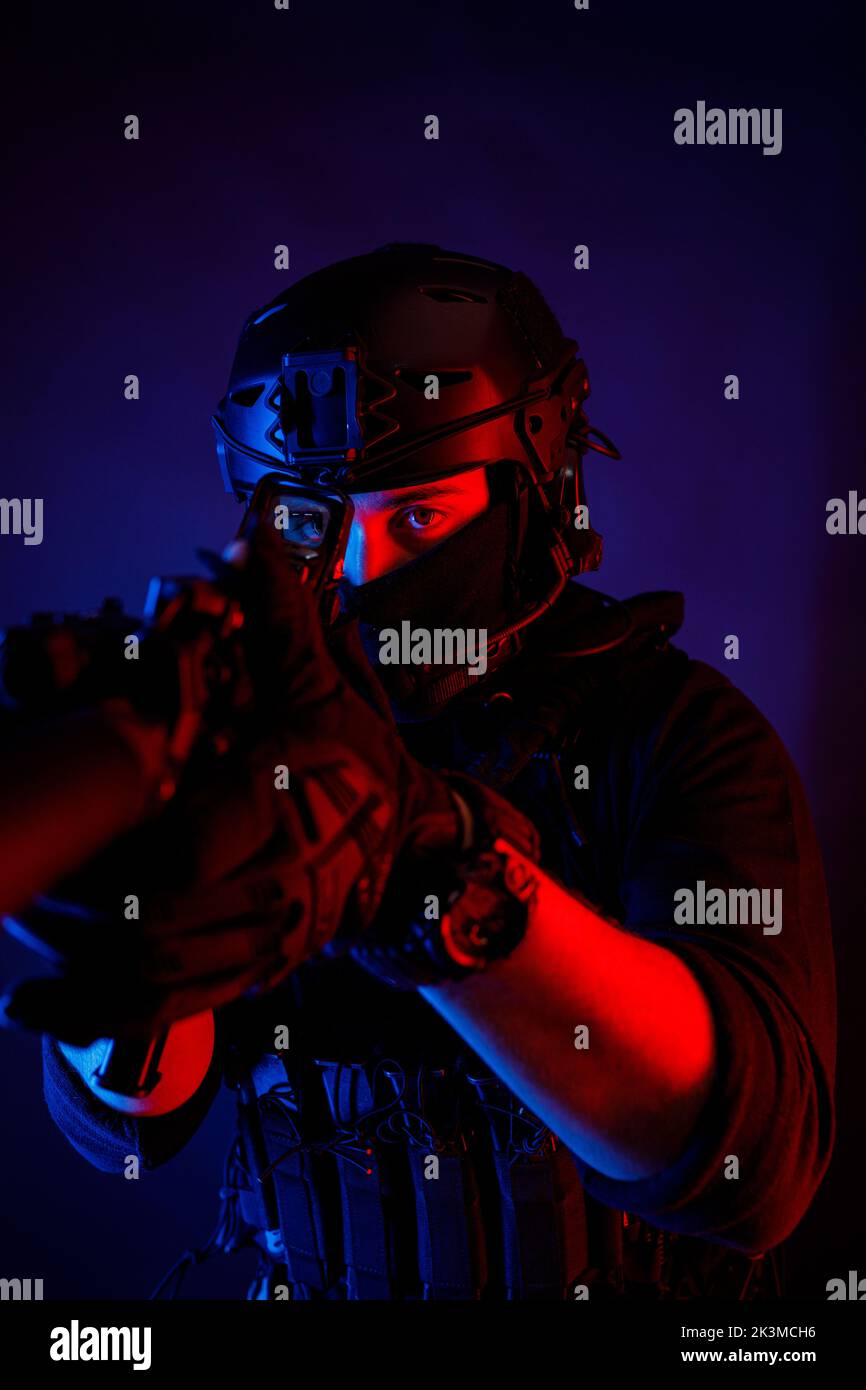 Méconnaissable un jeune homme attentif dans un équipement de combat et un casque de protection regardant la caméra à travers la lentille du fusil tout en prenant le but dans une pièce sombre Banque D'Images