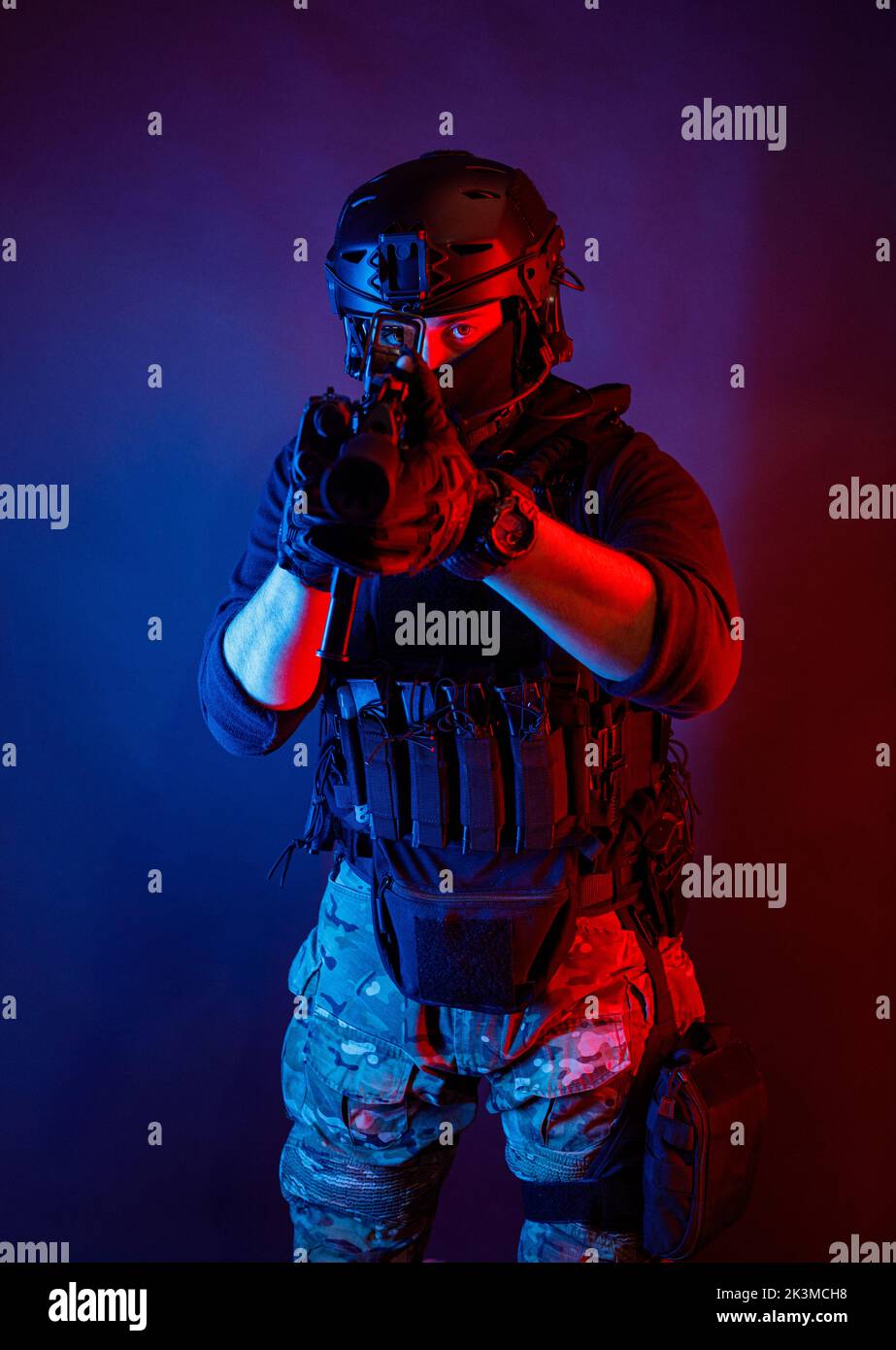 Méconnaissable un jeune homme attentif dans un équipement de combat et un casque de protection regardant la caméra à travers la lentille du fusil tout en prenant le but dans une pièce sombre Banque D'Images