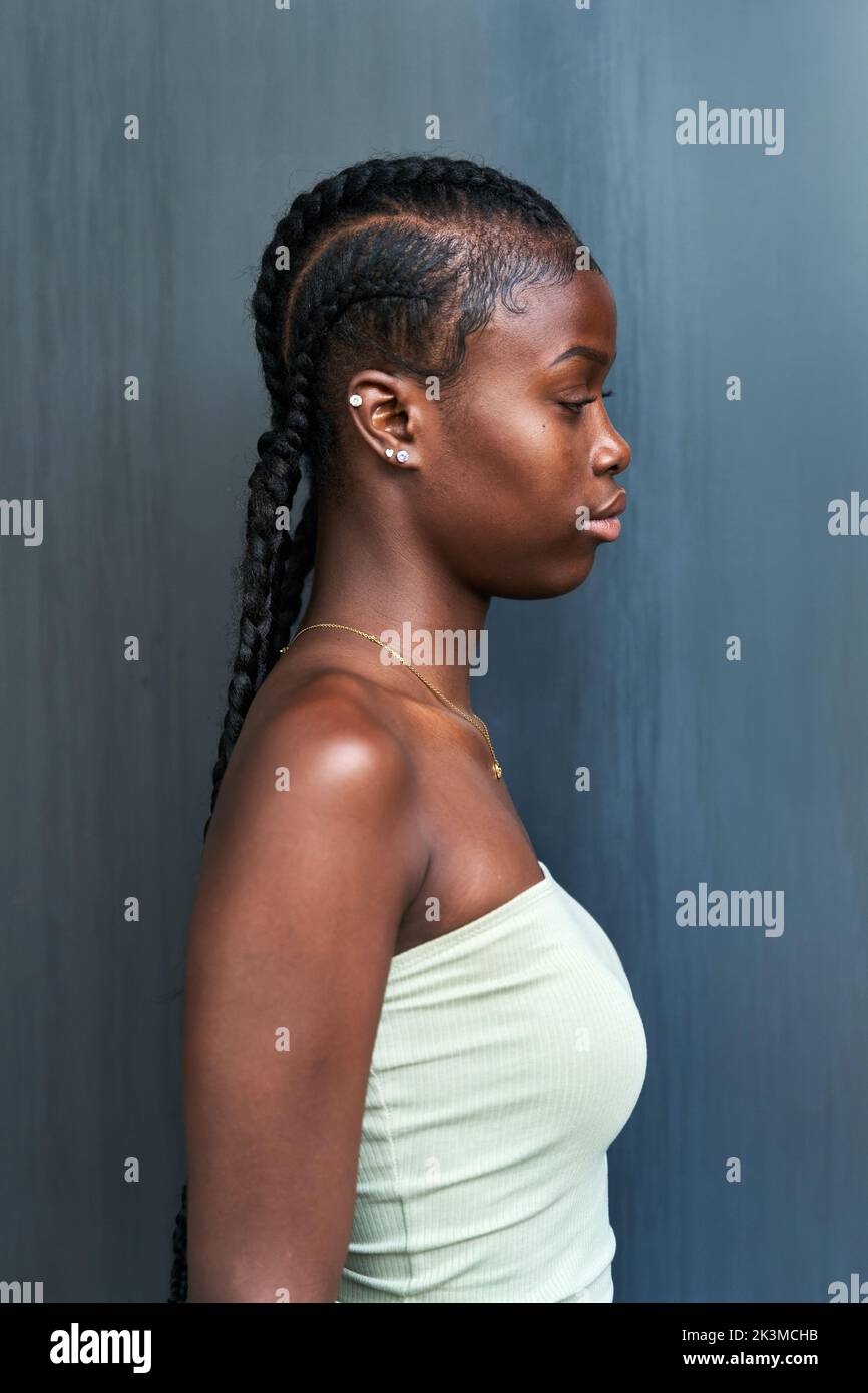 Vue latérale jeune femme afro-américaine avec de longues tresses portant un tube et regardant loin sur fond gris Banque D'Images
