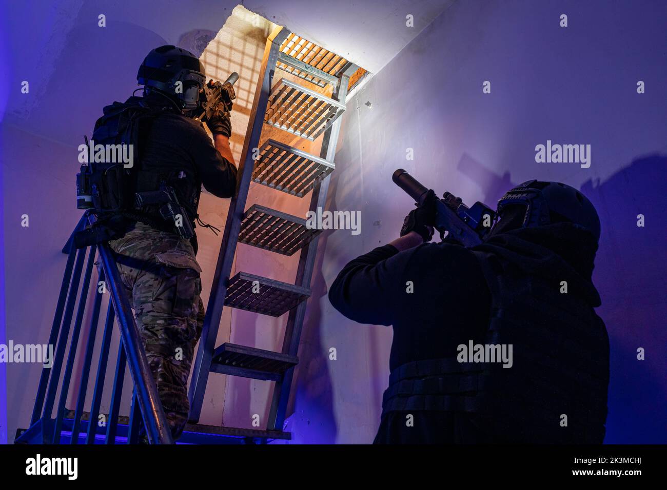 Vue arrière de soldats mâles méconnus dans un équipement de protection et un casque debout sur un escalier et en train de viser avec des fusils Banque D'Images