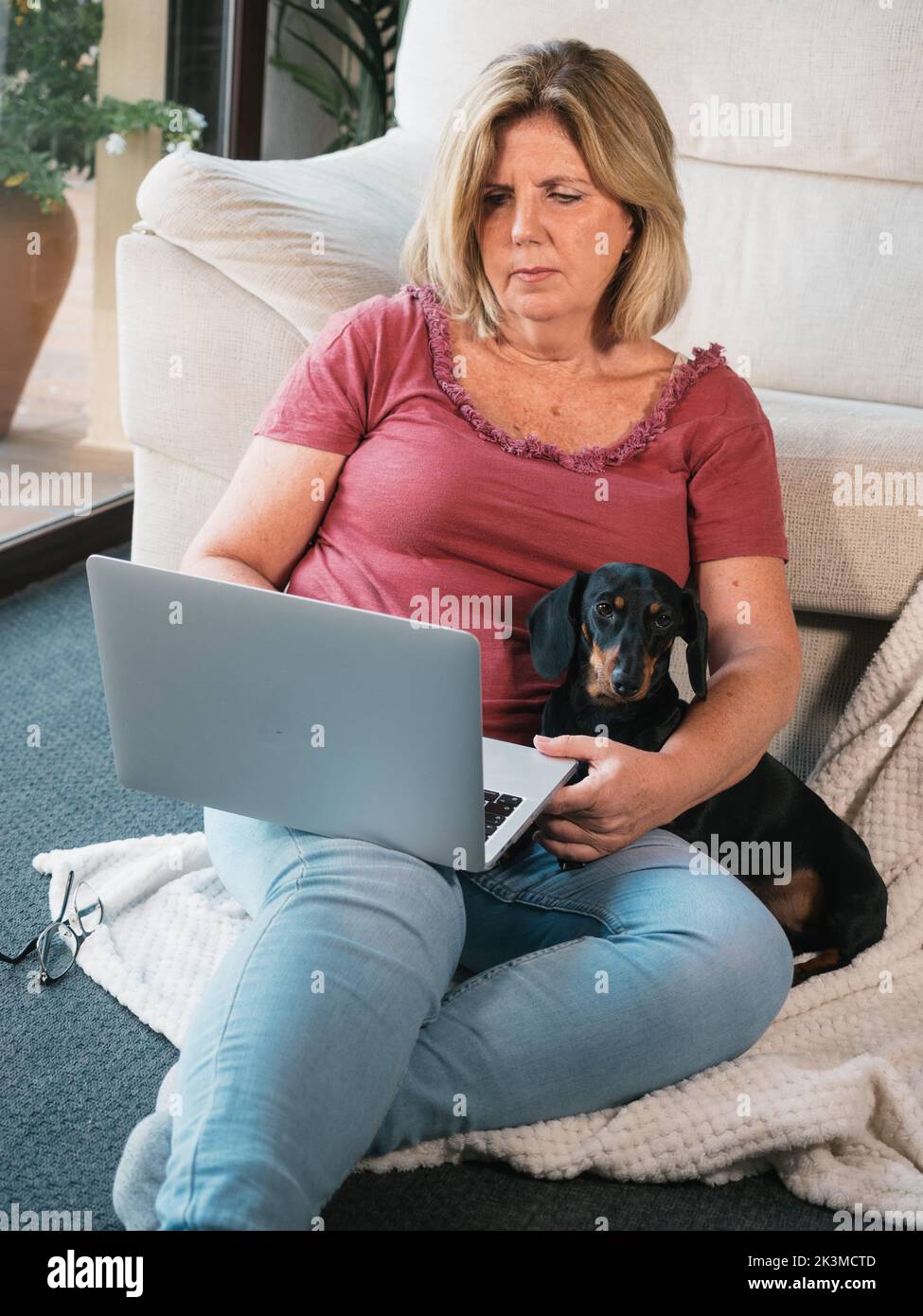 Femme mature caucasienne travaillant à la maison avec un ordinateur et son chien de Dachshund Banque D'Images