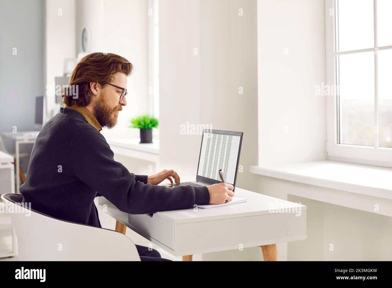 Homme sérieux au bureau travaillant avec des bases de données à l'aide d'un ordinateur portable et d'une feuille de calcul Excel. Banque D'Images