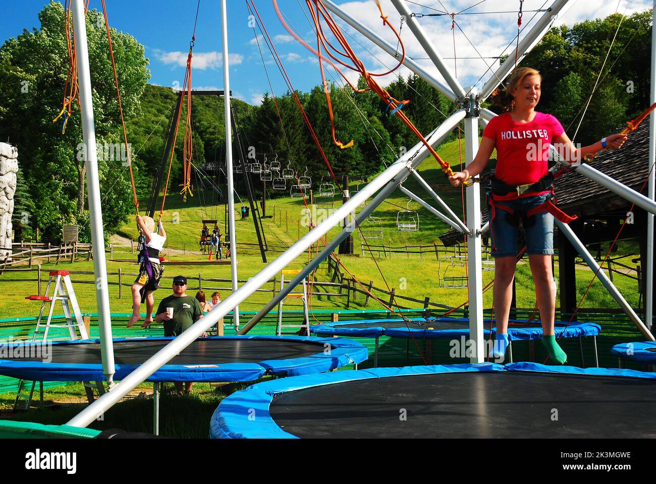 Une jeune femme adulte, attachée à des cordes de bungie, tente de sauter plus haut sur un trampoline, ouvert dans une station de ski pendant l'été hors saison Banque D'Images