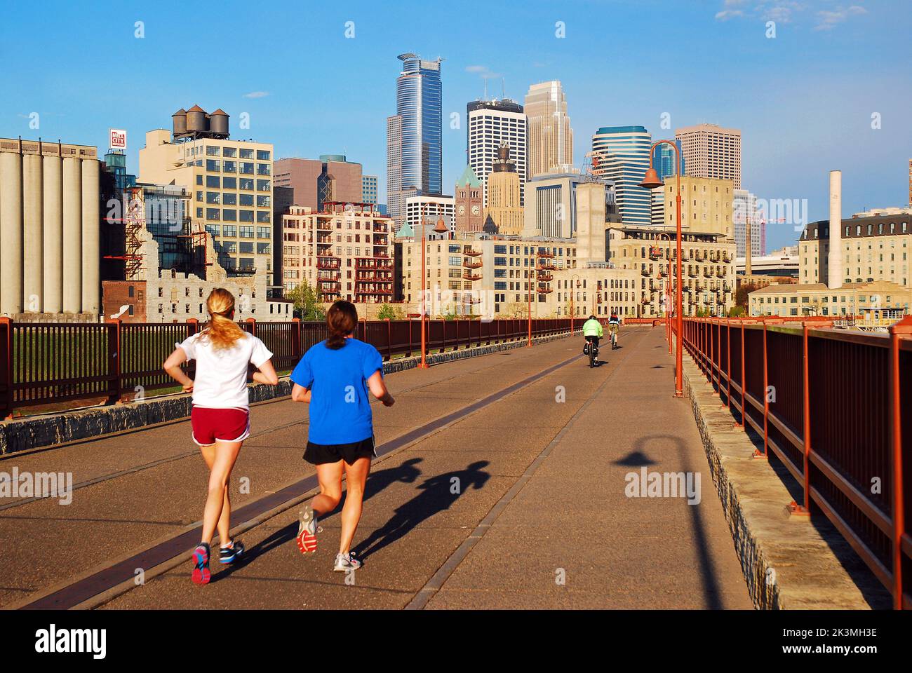 Deux joggeurs pour femmes profitent d'un style de vie sain en traversant le pont Stone Arch en direction de Minneapolis, Minnesota Banque D'Images