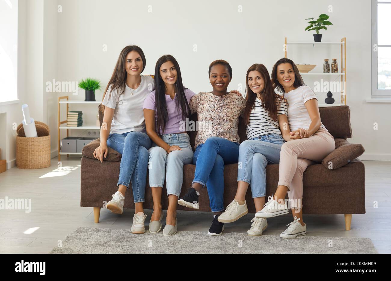 Groupe de jeunes femmes souriantes assises sur un canapé tout en restant à la maison ensemble Banque D'Images