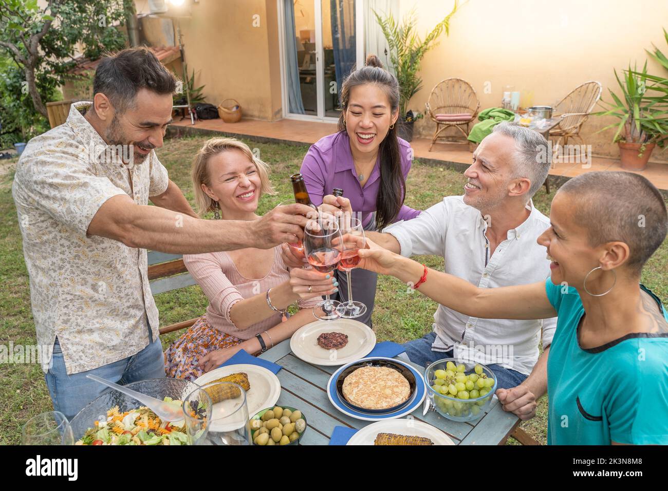 Groupe d'amis multiraciaux qui toasent avec un beau sourire autour de la table au patio de la maison. Banque D'Images