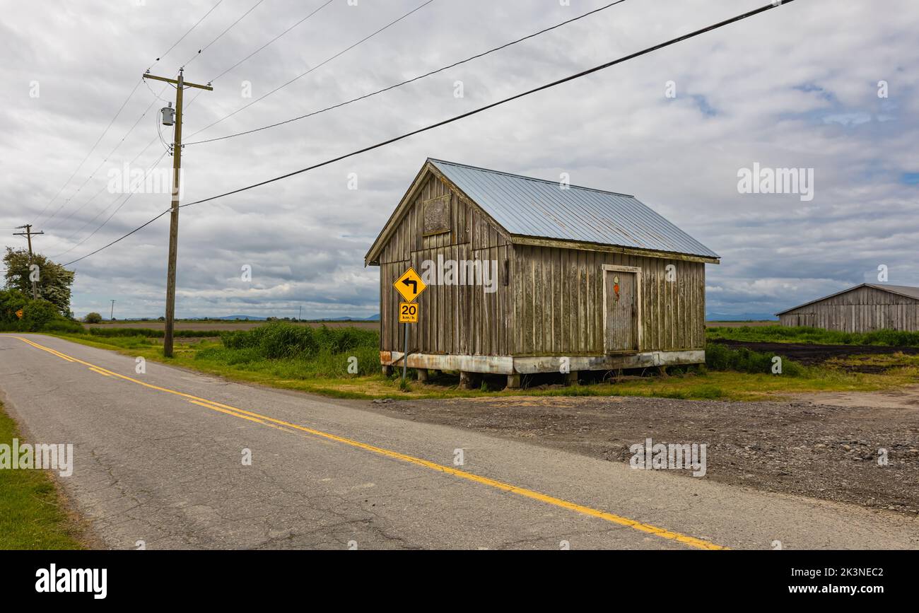 Ancienne ferme en bois dans la campagne au coucher du soleil avec nuages de tempête dans le ciel. Une vieille maison au bord de la route rurale. Personne, photo de voyage, photo de rue Banque D'Images