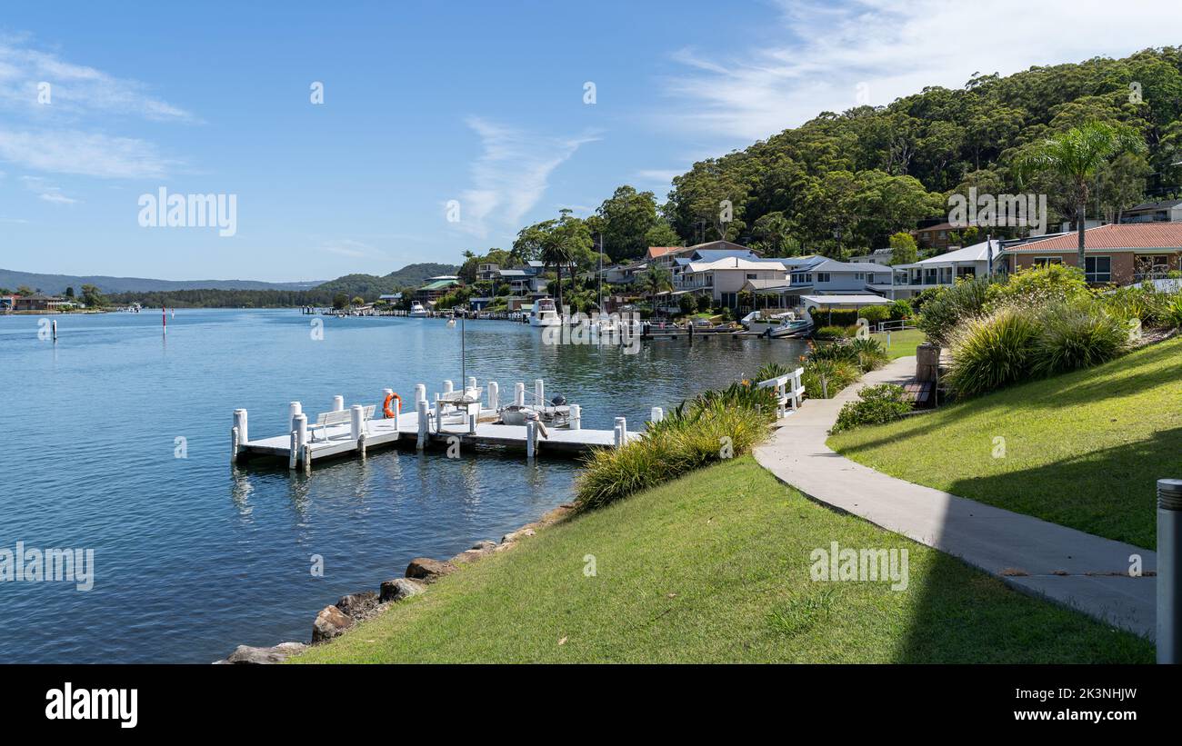 Belles maisons australiennes en bord de mer sur la colline. Village de pêcheurs. Petit quai ou jetée dans l'eau de mer bleue près d'un pré vert et d'une colline avec des arbres. Banque D'Images