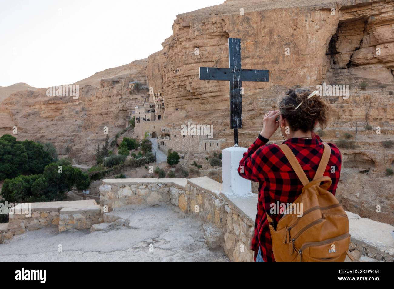 Une femme utilise des jumelles pour observer le monastère de Saint-Georges de Koziba, niché dans la vallée luxuriante du désert de Wadi Qelt, Judée ou Judée en Israël Banque D'Images