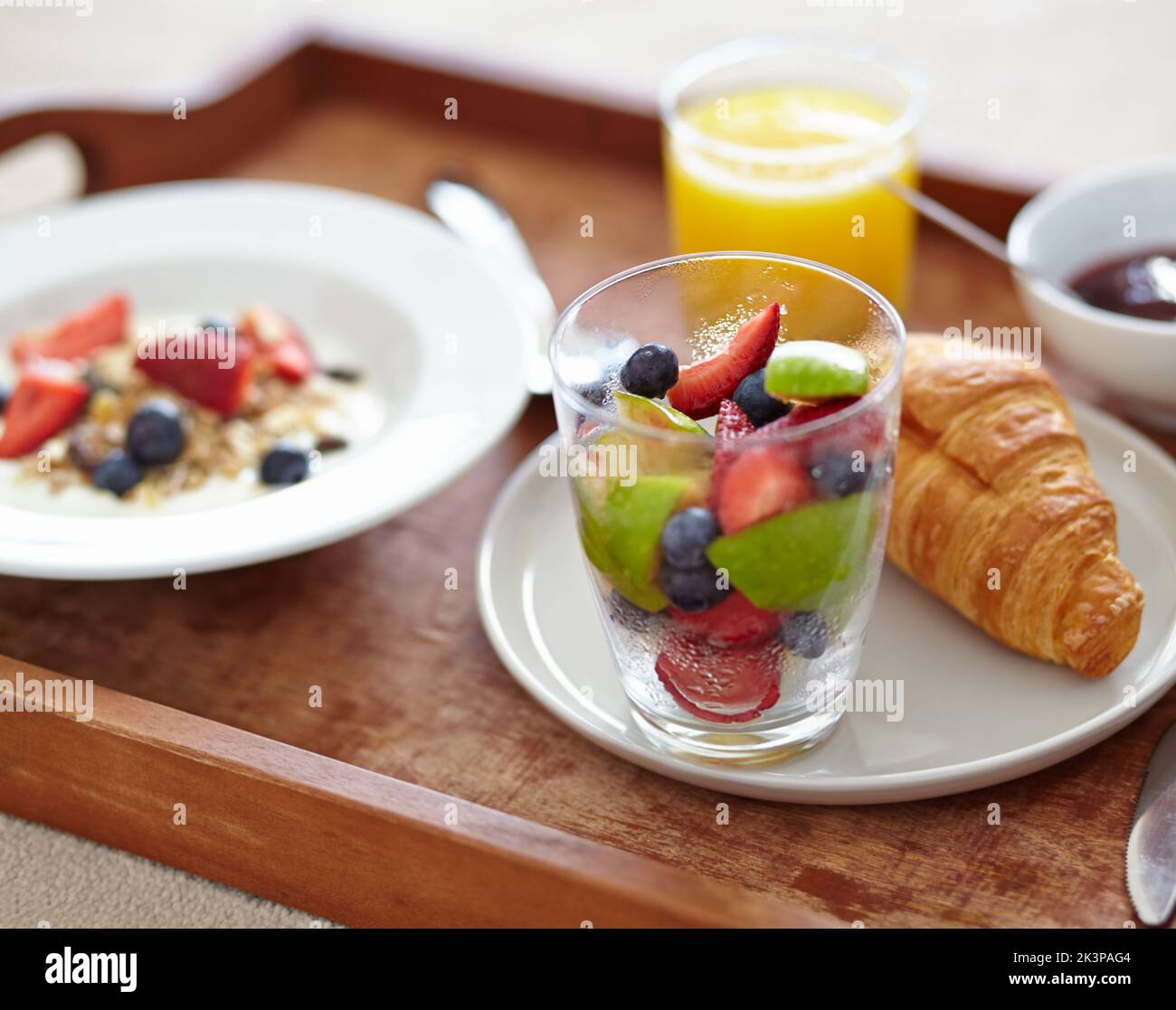 Nutritif et délicieux. Gros plan sur un plateau petit déjeuner avec jus de fruits, salade de fruits, croissant et muesli. Banque D'Images