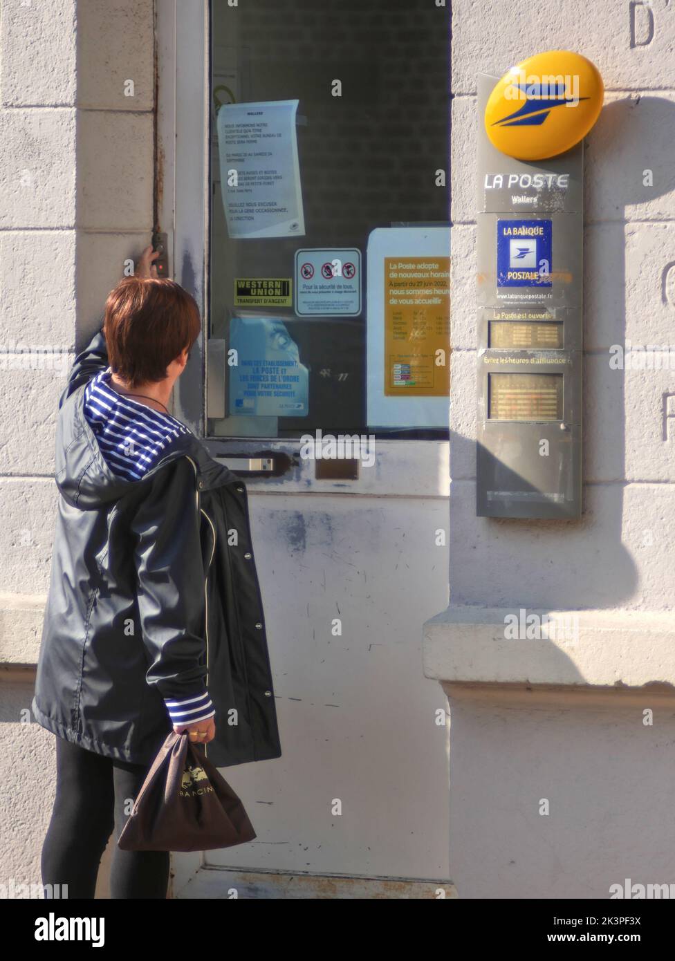 Wallers, France - 09 23 2022 : Femme caucasienne sonnant la sonnette du bureau de poste pour entrer. Banque D'Images