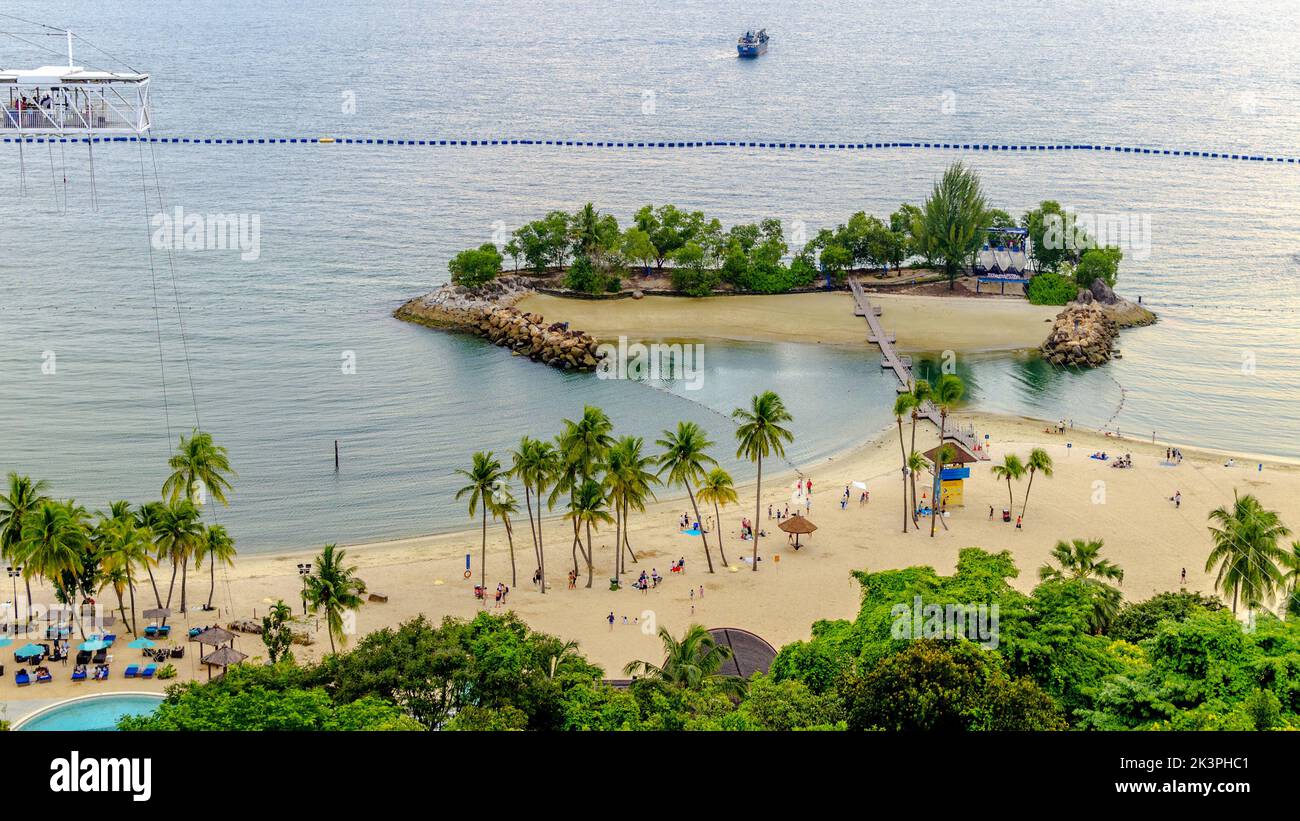 Vue aérienne de la plage de Siloso à Sentosa, Singapour. Les gens s'amusent sur le sable fin et les eaux calmes. Un pont suspendu relie à une petite île Banque D'Images