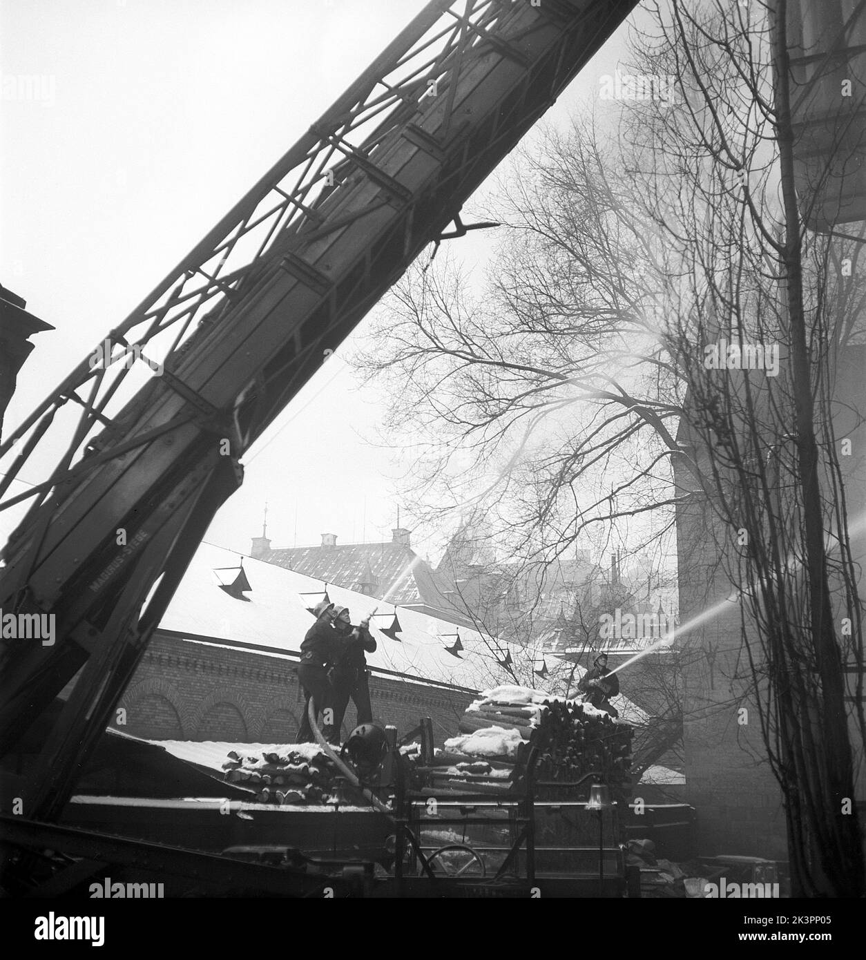 Incendie en 1940s. Les pompiers et les pompiers sont vus avec des tuyaux de pulvérisation d'eau sur un bâtiment en feu. C'est dans le centre de Stockholm en hiver. Suède 1945 Kristoffersson réf. M128-1 Banque D'Images