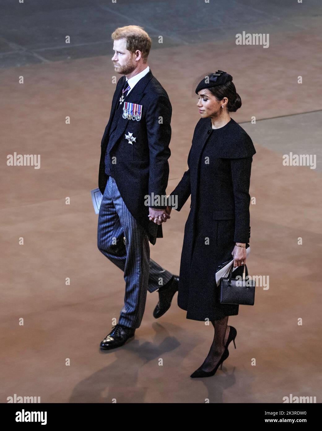 Le prince Harry et Meghan Markle tiennent les mains, le duc et la duchesse de Sussex quittent le service pour l'arrivée du cercueil de la reine Elizabeth II au palais de Westmin Banque D'Images