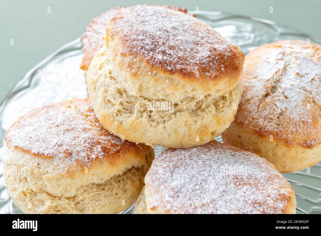 Des scones simples fraîchement confectionnés sont présentés sur un support à gâteau en verre. Les gâteaux sont légèrement saupoudrés de sucre glace et présentés en gros plan Banque D'Images