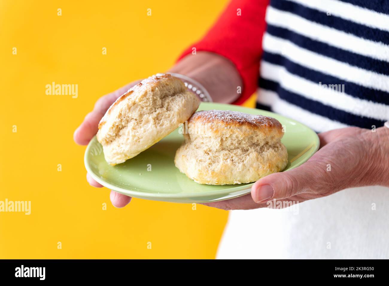 Une femme élégamment habillée est présentée avec deux scones simples fraîchement confectionnés sur une petite assiette. Les gâteaux sont légèrement saupoudrés de sucre glace Banque D'Images