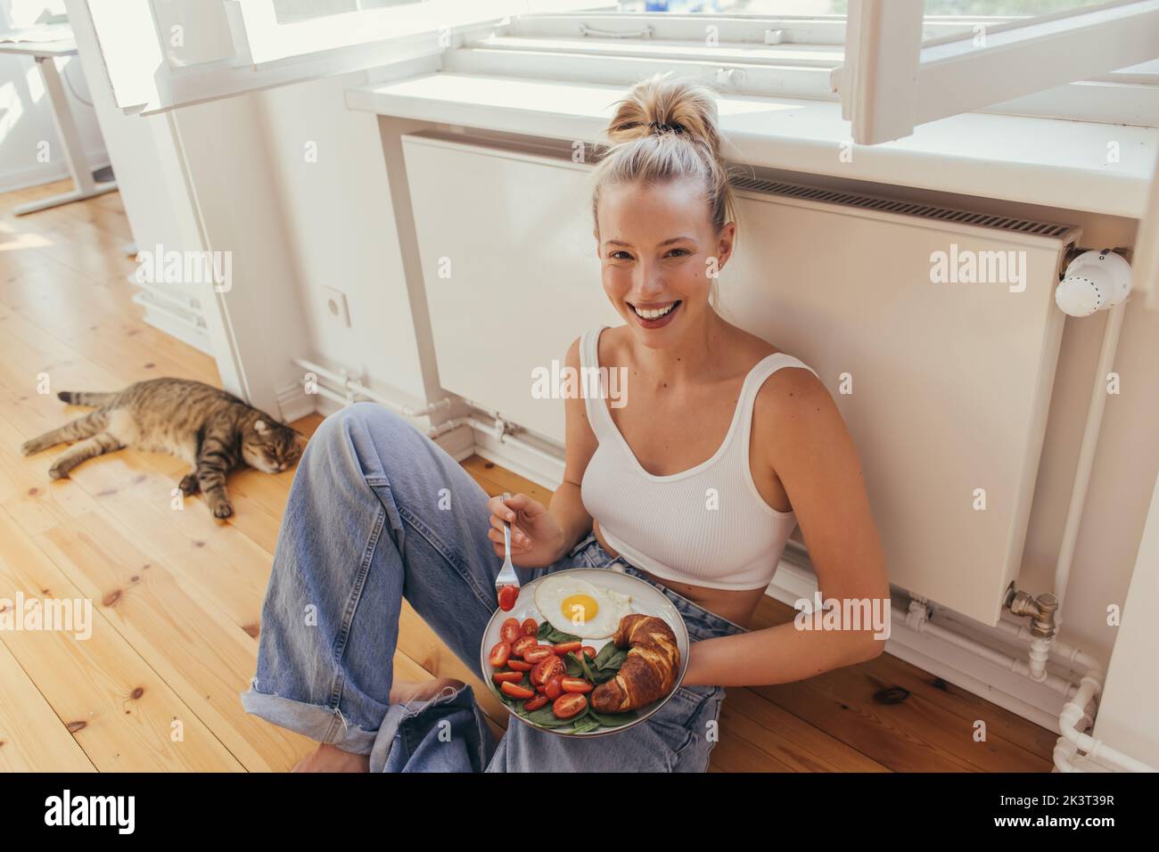 Femme souriante dans la plaque de maintien supérieure avec petit déjeuner savoureux près de flou scottish plient chat à la maison, image de stock Banque D'Images