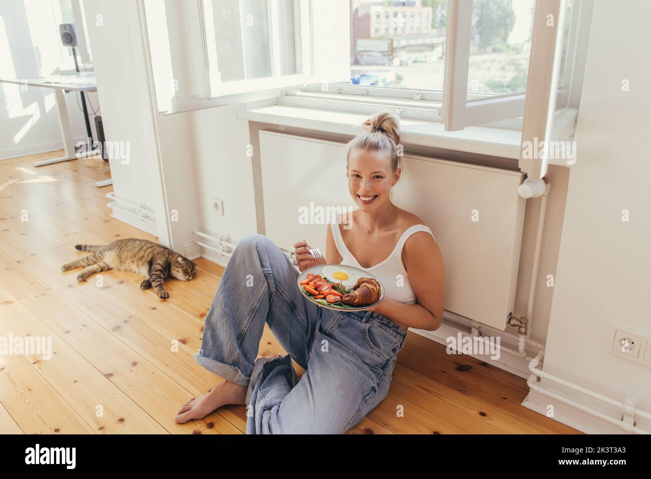 Jeune femme positive tenant une assiette avec un délicieux petit déjeuner près de scottish pli chat à la maison, image de stock Banque D'Images