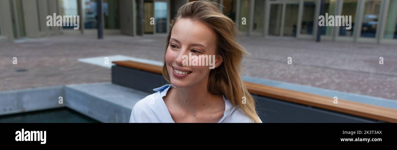 Femme blonde souriante regardant loin sur la rue urbaine, bannière, image de stock Banque D'Images