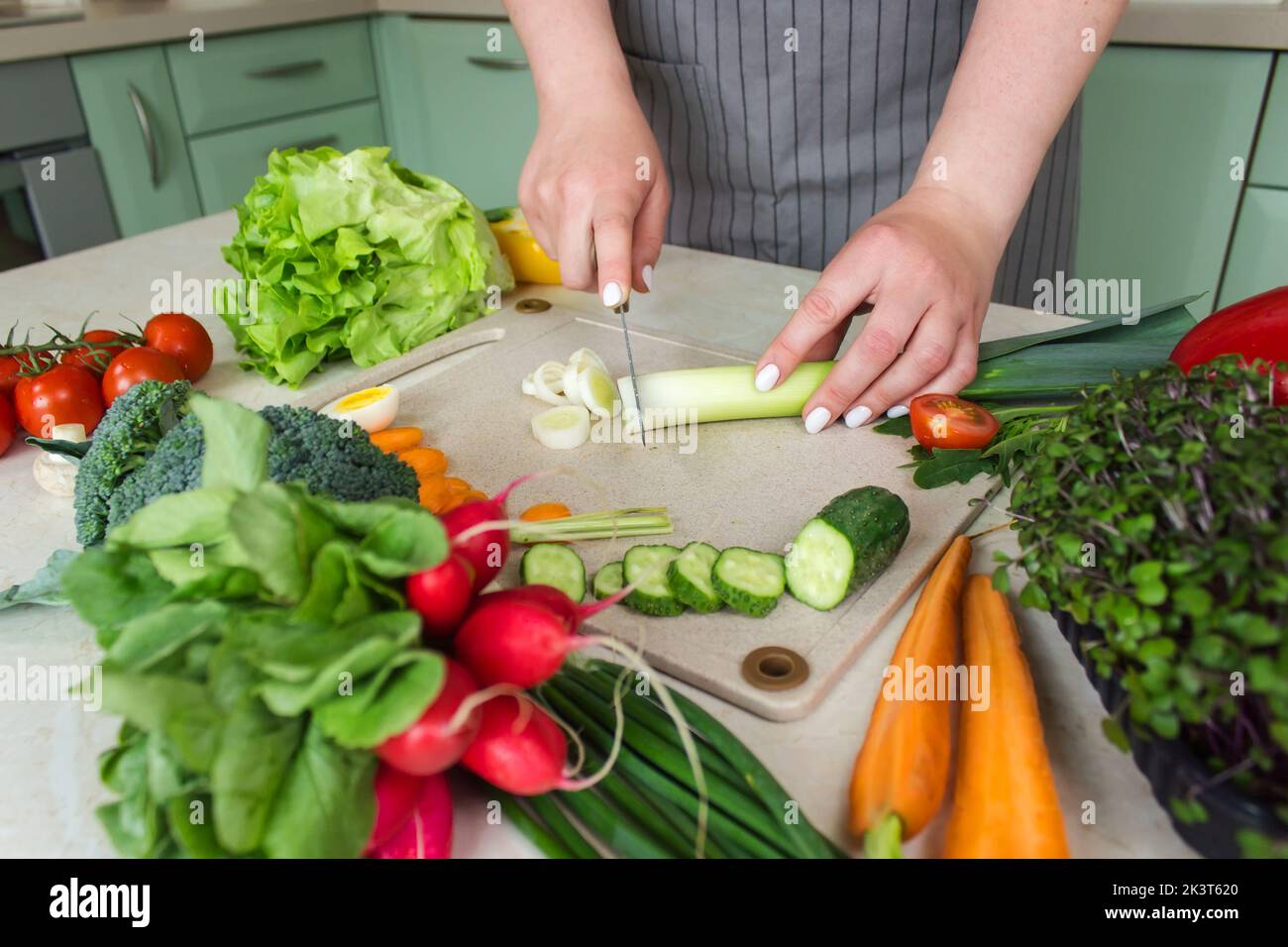 La femme prépare de la salade de légumes dans la cuisine et coupe des ingrédients sur la table. Aliments sains de légumes. Banque D'Images