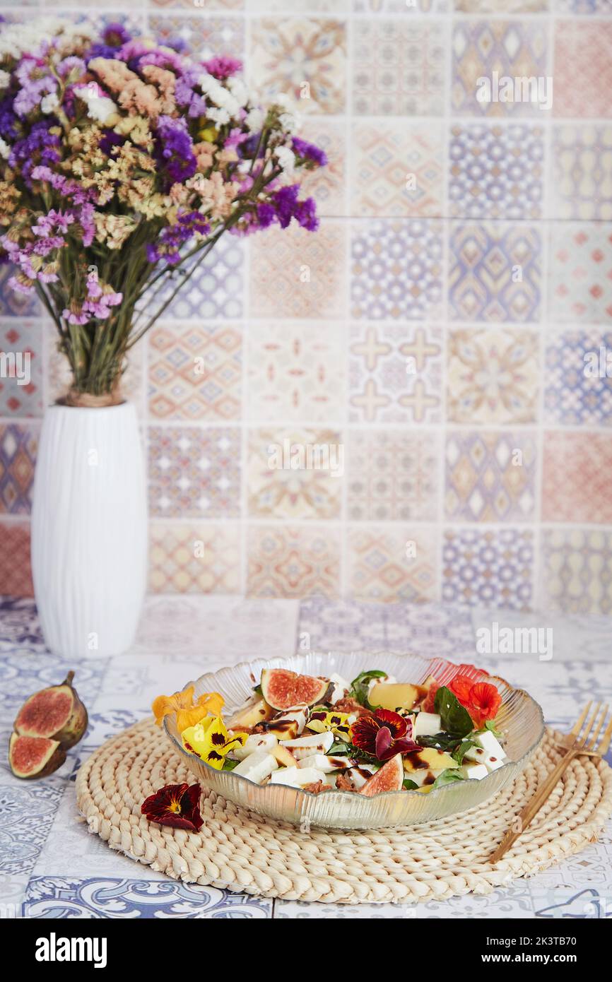 Dîner sain - salade avec feta, fleurs comestibles, figues, pêche, basilic sur fond de carreaux de céramique avec tournesols Banque D'Images