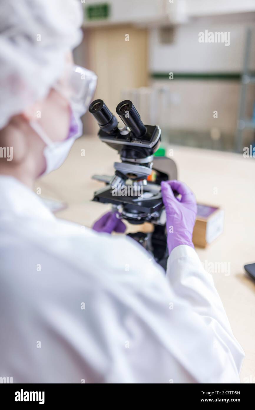 vue arrière d'une femme scientifique anonyme regardant au microscope en laboratoire Banque D'Images
