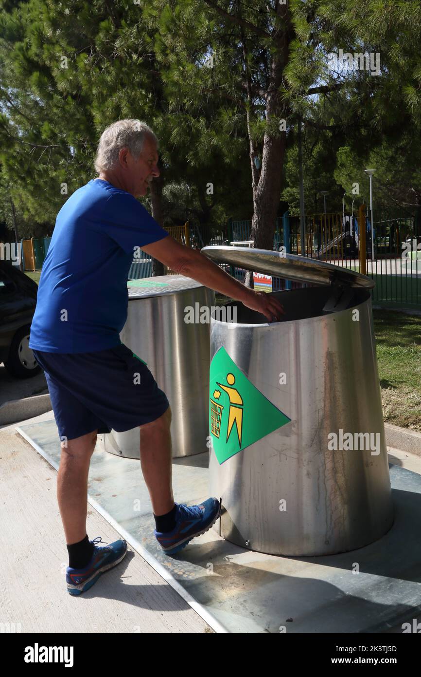 Vouliagmeni Athènes Grèce Thiseos Street Man mettant des ordures dans la poubelle de recyclage de pédales Banque D'Images