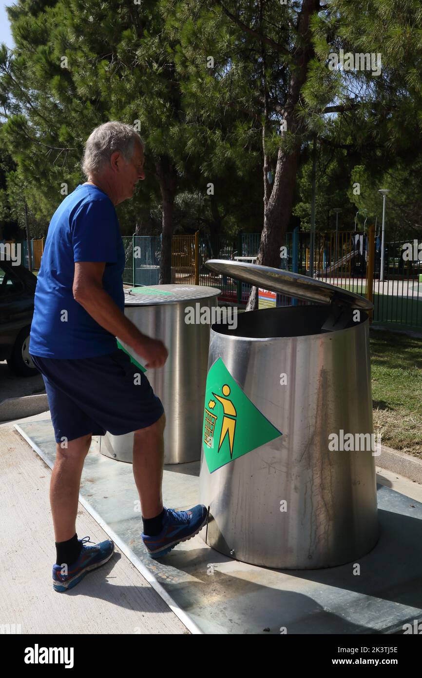 Vouliagmeni Athènes Grèce Thiseos Street Man mettant des ordures dans la poubelle de recyclage de pédales Banque D'Images