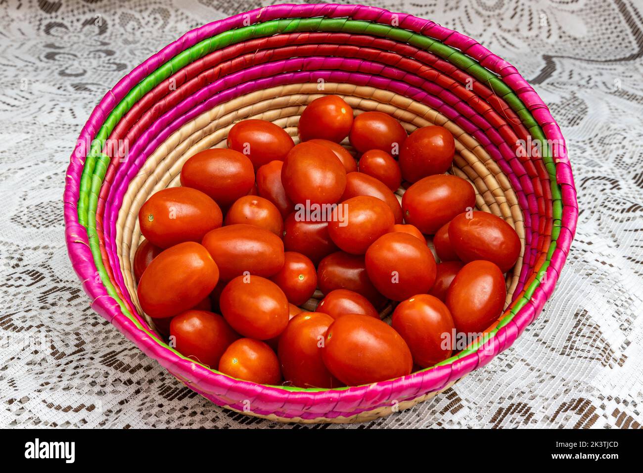 Groupe de tomates cerises dans un panier en osier mexicain sur une nappe tricotée fine brune, délicieux, rouge et biologique cultivé dans le jardin. Concept de bio, Banque D'Images