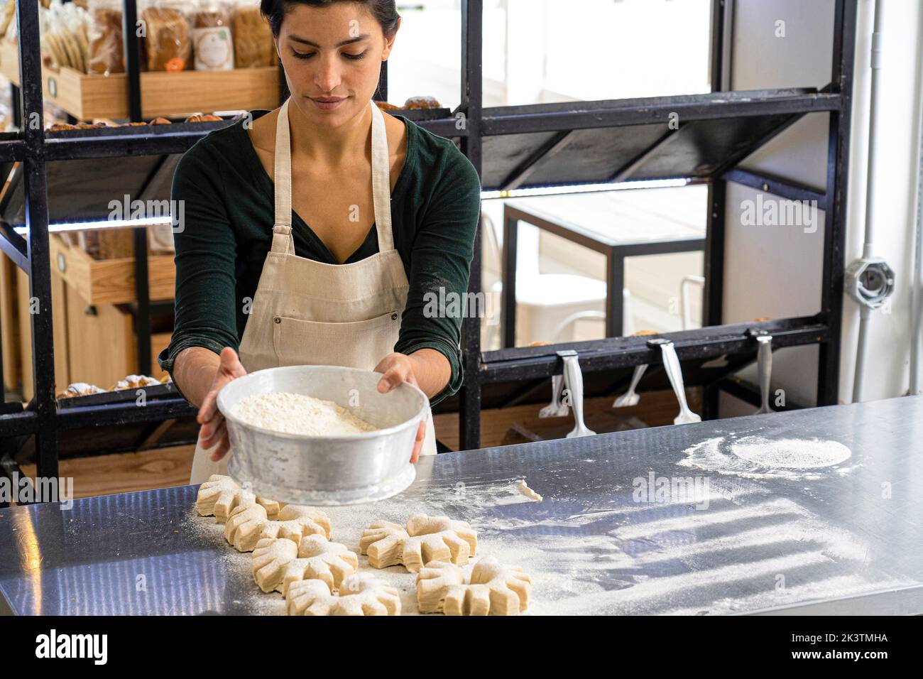 Dose moyenne de la propriétaire de boulangerie latino-américaine féminine qui a tamisé la farine sur ses pains Banque D'Images