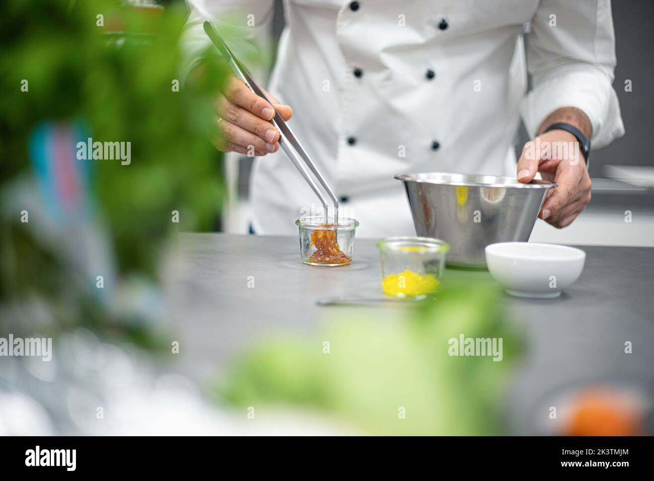 Croiser anonyme chef masculin en uniforme blanc debout près de la table avec des pinces et mélanger noix dans le miel de pot en verre près des ingrédients et bols dans léger ki Banque D'Images