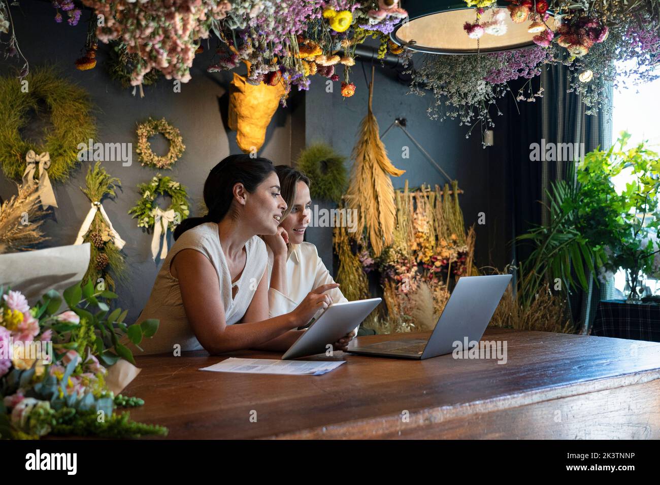Vue large de deux femmes différentes maison décoration propriétaires de magasin travaillant avec un ordinateur portable et une tablette numérique Banque D'Images