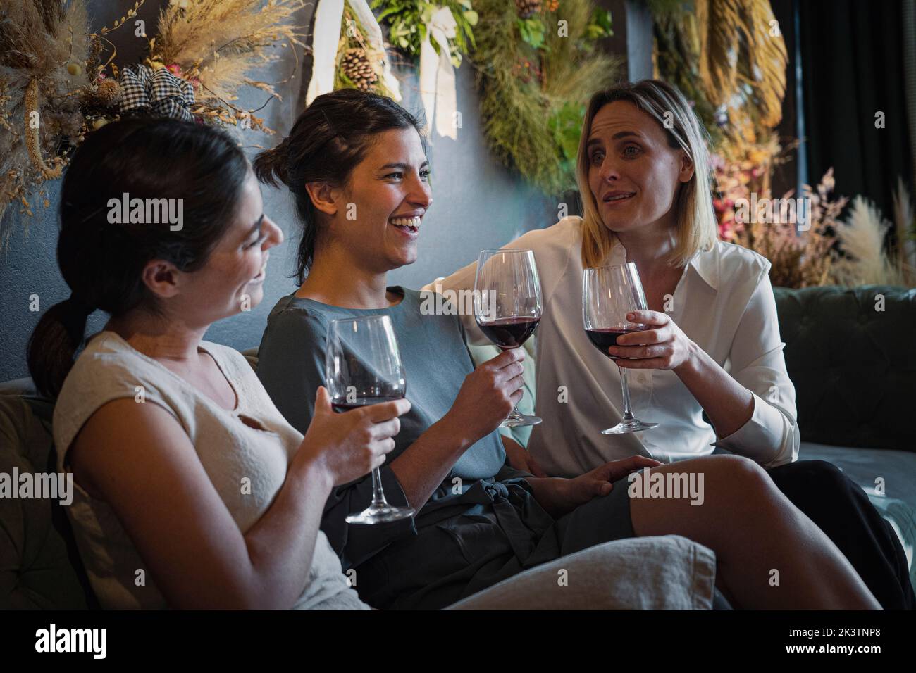 Portrait de groupe de trois amies féminines joyeuses et variées qui se traînaient tout en buvant du vin au bar à vins à la mode Banque D'Images