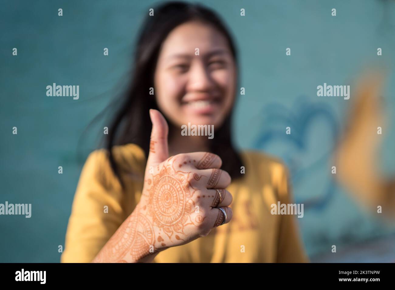 Heureuse femme ethnique debout dans la rue par beau temps avec les mains peintes de henné et montrant le pouce vers le haut geste Banque D'Images