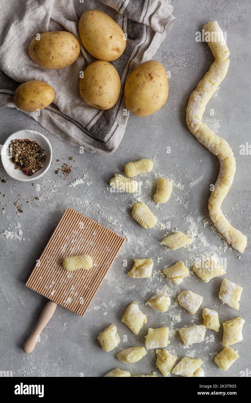 De dessus vue de dessus de dessus de gnocchi non cuit avec pomme de terre et poivre placé près du couteau et de la planche striée sur la table grise pendant la préparation du déjeuner dans la cuisine Banque D'Images