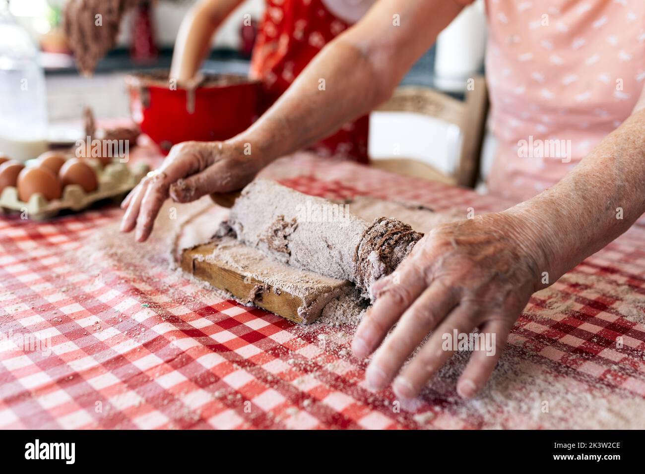 Grand-mère anonyme contre petite-fille méconnue avec de la pâte sur les mains pendant le processus de cuisson à la table dans la cuisine de la maison Banque D'Images
