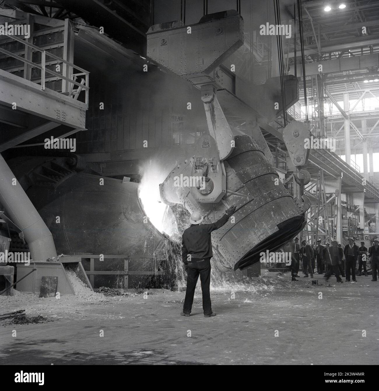 années 1950, historique, fabrication de l'acier.... À l'intérieur d'un hangar industriel géant, un ouvrier de l'acier supervisant un grand baril de minerai de fer fondu versé dans un haut fourneau de la Steel Company of Wales, Abbey Works, Port Talbot, pays de Galles, Royaume-Uni. Banque D'Images