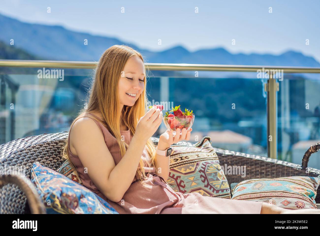 Portrait d'une femme magnifique portant une belle robe assise dans un patio et mangeant de la fraise Banque D'Images
