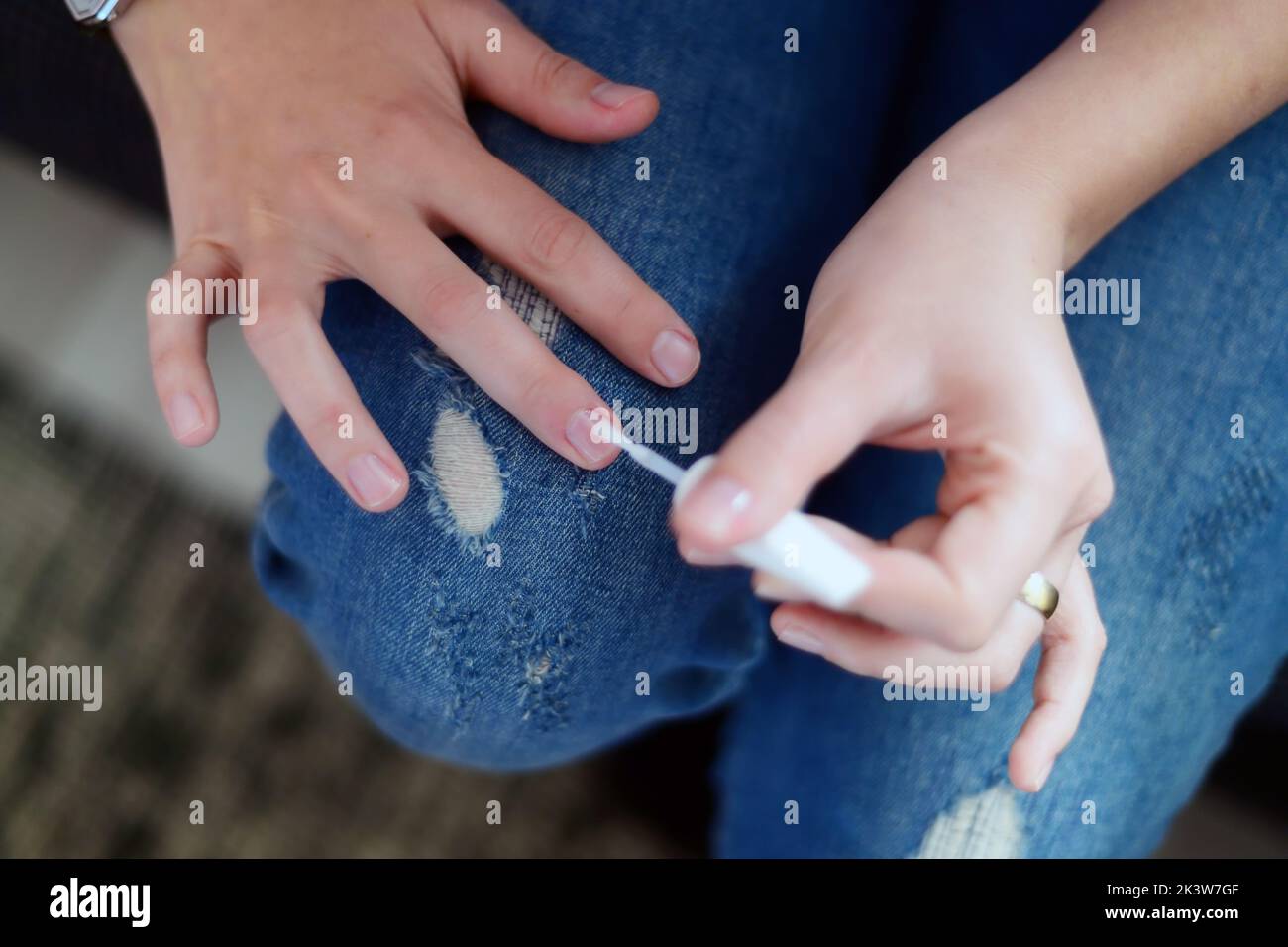 Un gros plan d'une femme peignant ses ongles avec un manteau de dessus transparent Banque D'Images