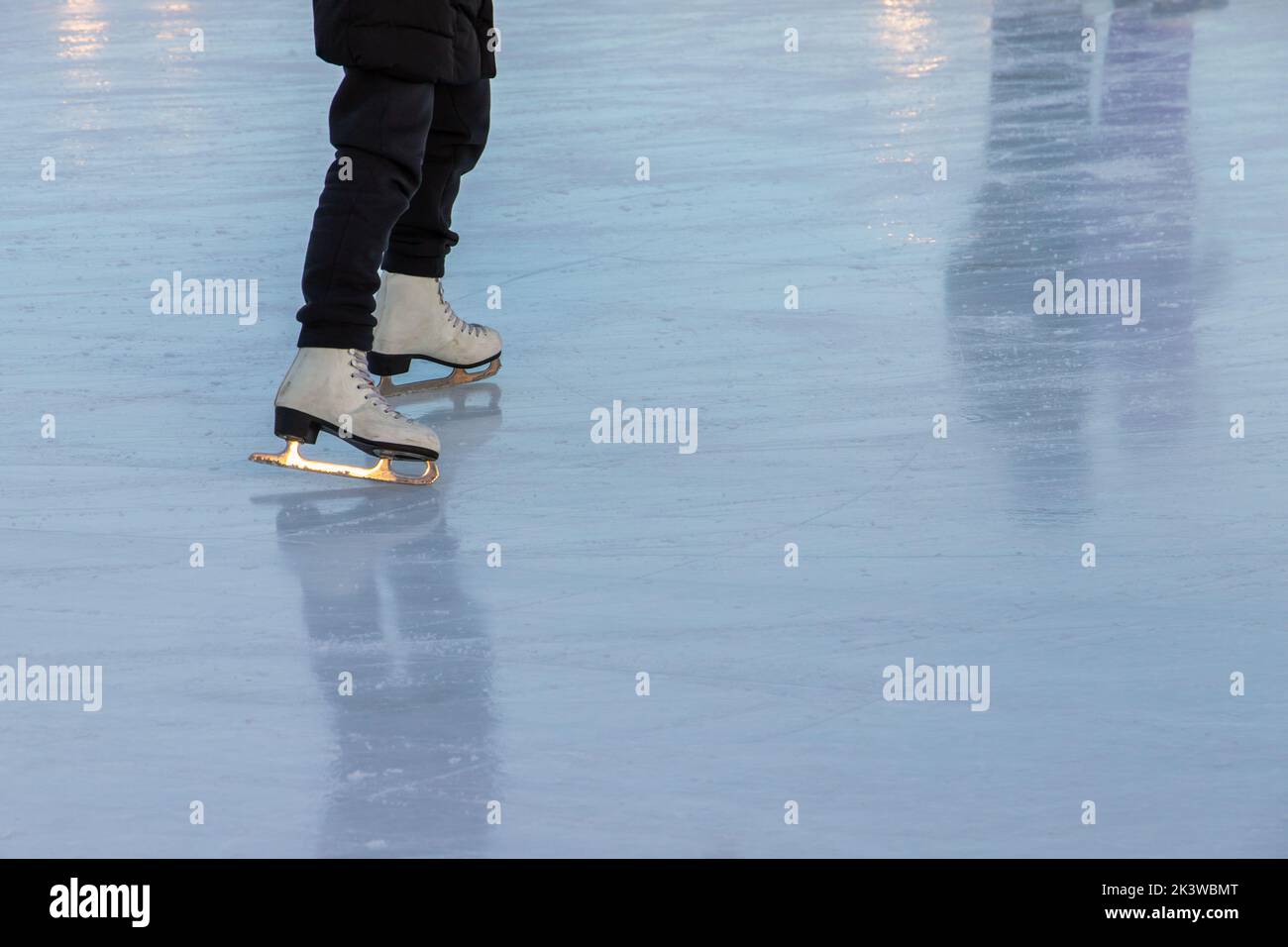 Jambes d'une fille sur patins sur une patinoire brillante Banque D'Images