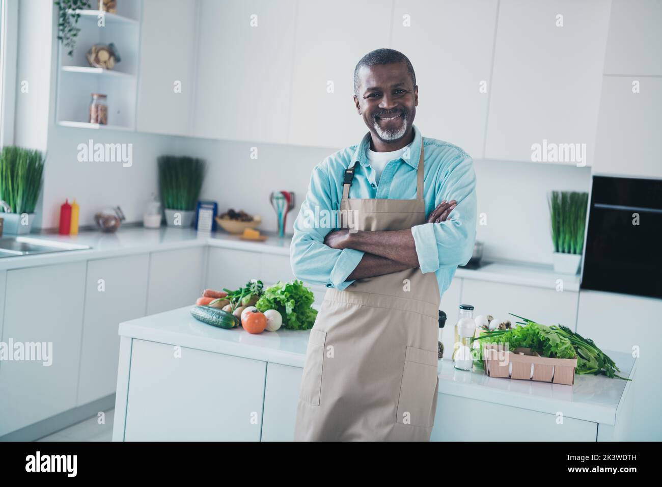Photo de l'homme vieillie positif croisant les bras prêt à préparer un savoureux souper produits bio frais dans la cuisine moderne maison Banque D'Images