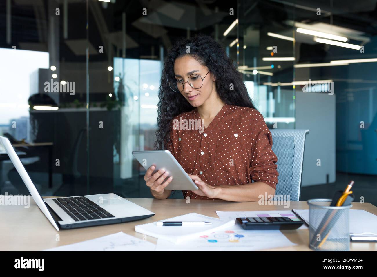 Jeune femme d'affaires prospère travaillant dans un immeuble de bureaux moderne, femme hispanique utilisant un ordinateur tablette souriante et heureuse. Banque D'Images