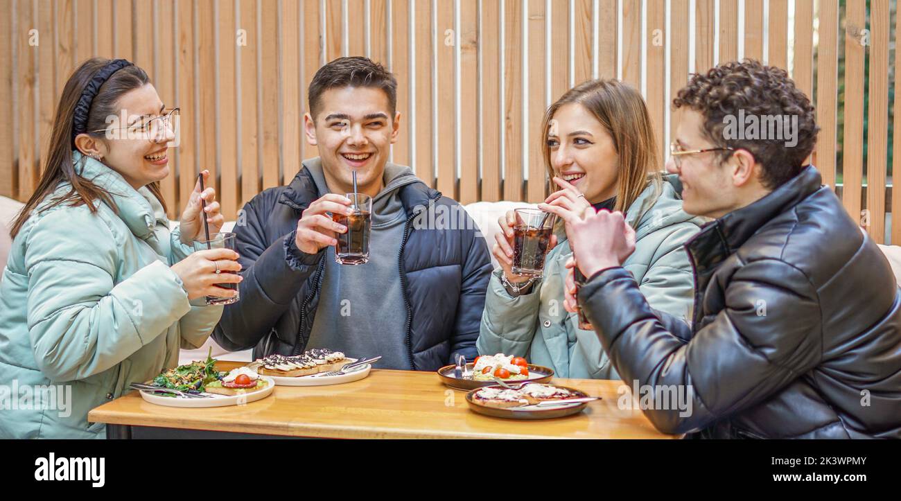 Groupe d'adolescents qui s'amusent à boire et à prendre un brunch à l'extérieur - les jeunes parlent et rient en sirotant de la nourriture dans un bar Banque D'Images