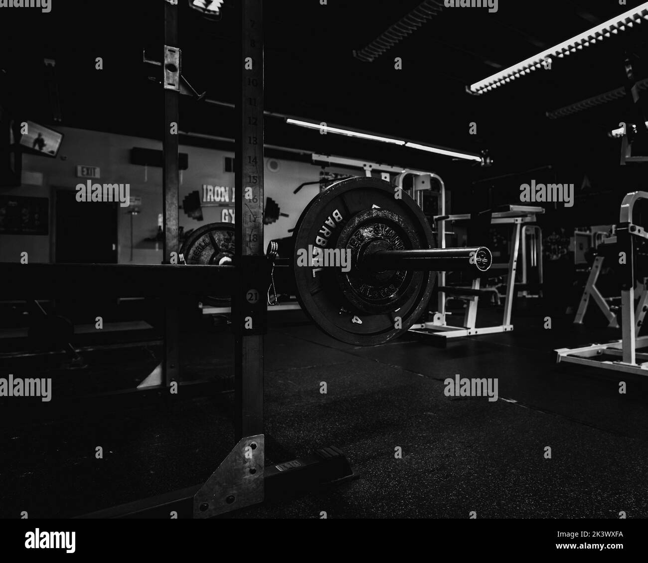 Une salle de gym en niveaux de gris avec vue à l'intérieur avec une barbell et d'autres pièces d'équipement autour Banque D'Images