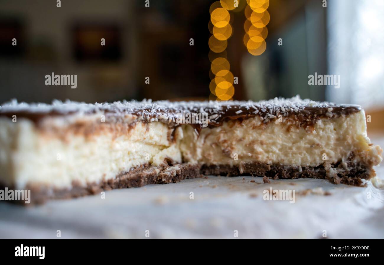 Gâteau de Bounty fait maison avec lait de coco et crème au chocolat sur une assiette blanche avec une cuillère contre la lumière de bokeh Banque D'Images